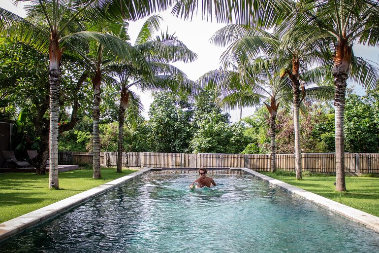 男子在两边种有棕榈树的泳池里游泳