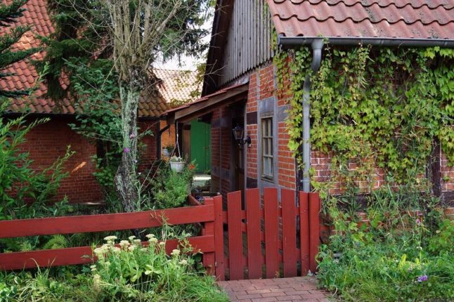 房子一侧的红褐色栅栏和大门，房子的砖上长着许多绿色植物和常春藤。