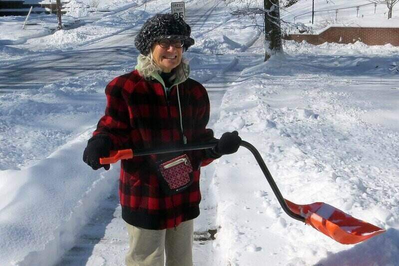 一名女子拿着雪铲站在干净的人行道上