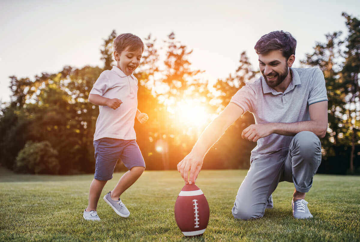 英俊的爸爸和他可爱的小太阳正在绿色的草坪上玩美式足球